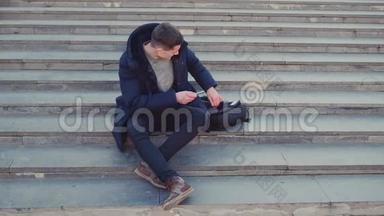 一个年轻人坐在楼梯上使用他的智能手机。 然后他就要把焦点放出来了。 复制空间。 行动